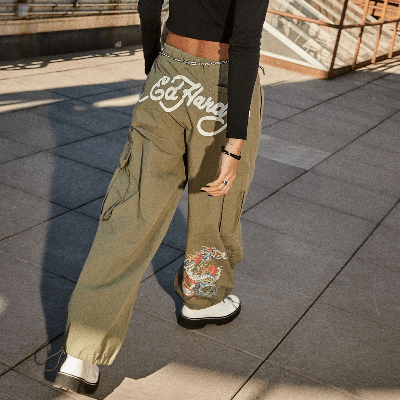 Woman wearing olive green Ed Hardy cargo pants with a dragon graphic on the leg and chain belt detail.