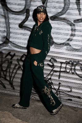 Woman in a dark green Ed Hardy fleece set with gold rose graphics, posing by a graffiti-covered shutter.