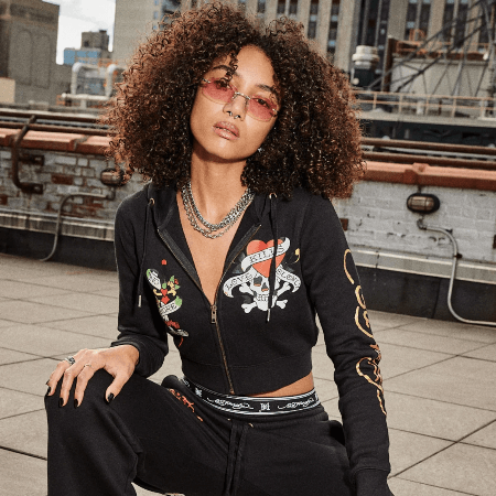 Ed Hardy women's black cropped zip hoodie with Love Kills Slowly skull graphic, worn on urban rooftop.