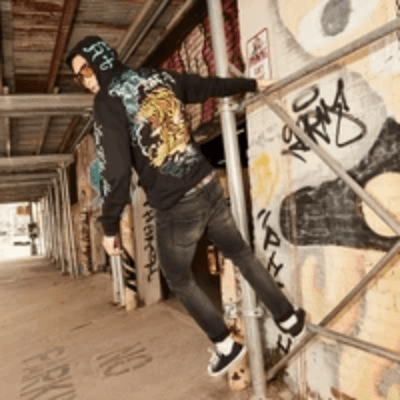 Man in a black Ed Hardy tiger graphic hoodie posing on scaffolding beside a graffiti-covered wall. Man in a black Ed Hardy tiger graphic hoodie posing on scaffolding beside a graffiti-covered wall.