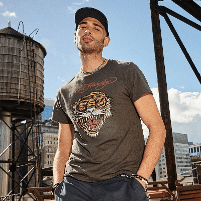 Man on a rooftop wearing a gray Ed Hardy T-shirt featuring a roaring tiger head graphic. Man on a rooftop wearing a gray Ed Hardy T-shirt featuring a roaring tiger head graphic.