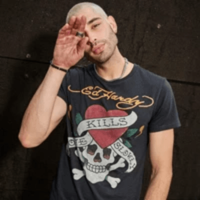 Man with bleached hair in a gray Ed Hardy T-shirt featuring a rhinestone skull graphic reading "Love Kills Slowly." Man with bleached hair in a gray Ed Hardy T-shirt featuring a rhinestone skull graphic reading "Love Kills Slowly."