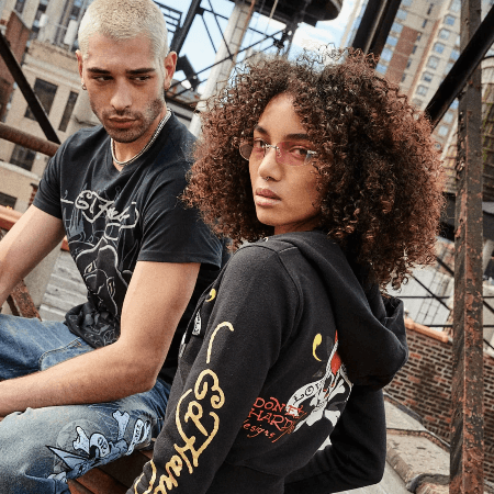 Two models in Ed Hardy graphic tee and hoodie posing on urban rooftop with city skyline backdrop.