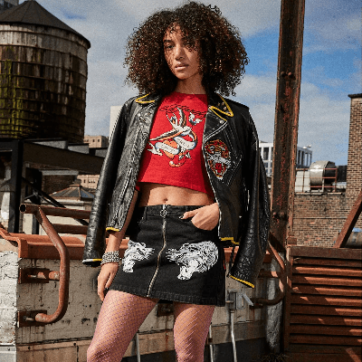 Woman on a rooftop in a red Ed Hardy graphic crop top, black denim mini skirt, and studded leather jacket. Woman on a rooftop in a red Ed Hardy graphic crop top, black denim mini skirt, and studded leather jacket.