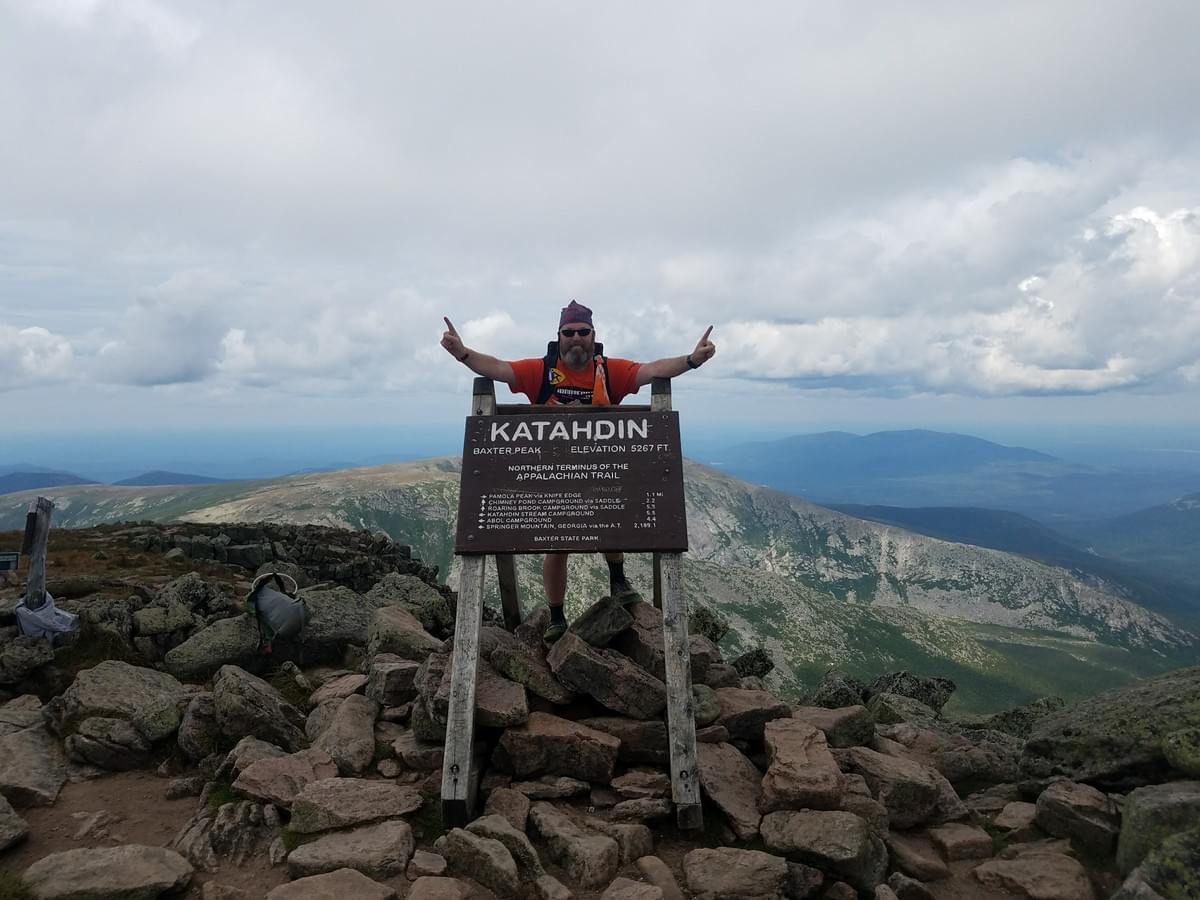 John Ironheart Kolker on the Katahdin summit sign, arms raised, finishing the Appalachian Trail