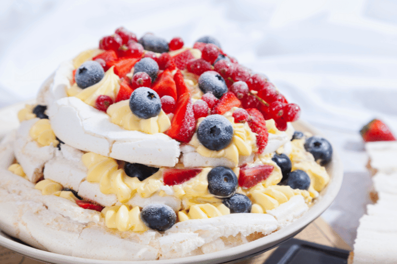 A multi-layered pavlova stack filled with yellow custard and fresh berries, showcasing the contrast between the white meringue and colorful fruit.