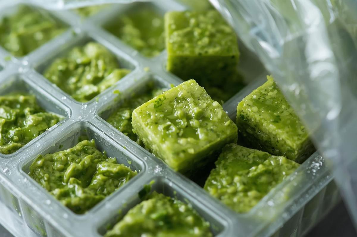 Close-up of bright green homemade ramp pesto cubes frozen in a plastic ice cube tray for long-term storage, showing the minced garlic and herb texture.