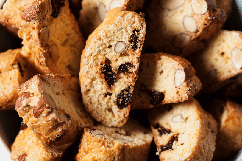 A bowl of golden-brown biscotti packed with almonds and dried fruit sits invitingly, showcasing their rustic texture and twice-baked crunch—perfect for pairing with coffee or gifting during the holidays.
