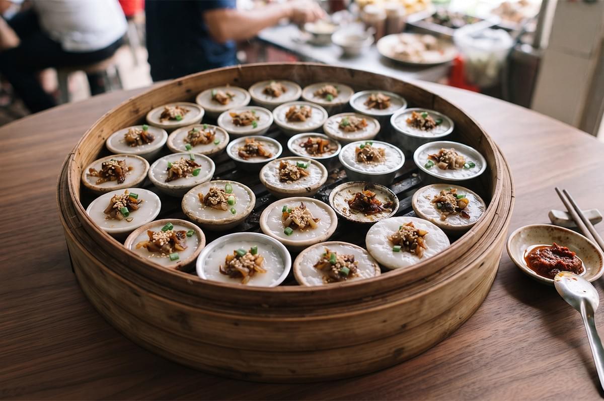 Freshly steamed Chwee Kueh rice cakes in small moulds inside a bamboo steamer with preserved radish toppings.