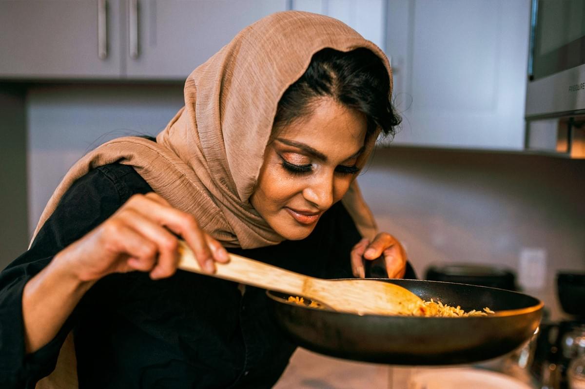 Person stirring and smelling a rice dish in a frying pan in a home kitchen, with steam rising from the food.