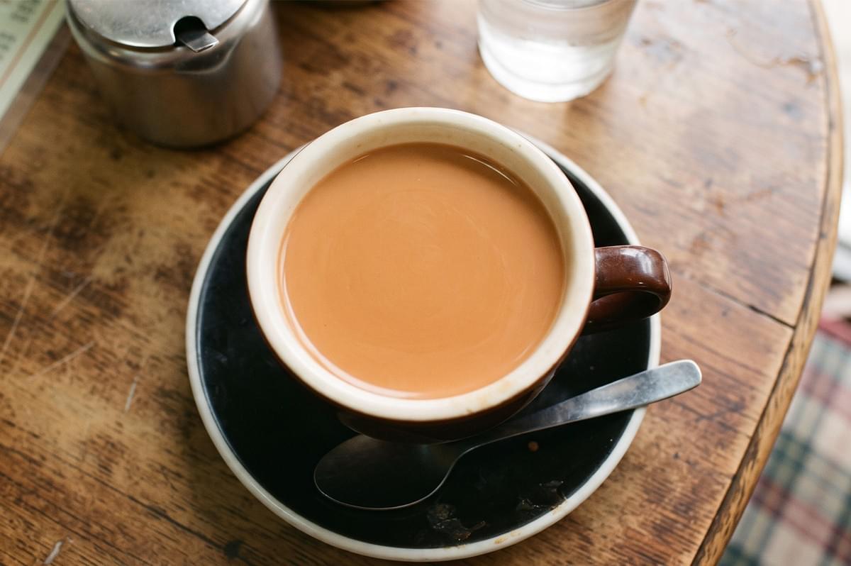 A ceramic cup of Hong Kong style milk tea mixed with coffee (Yuenyeung) on a wooden table with a saucer and spoon.