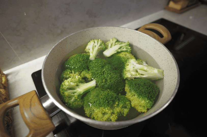 Broccoli florets submerged in a pot of hot water during the initial blanching stage to brighten their green color.