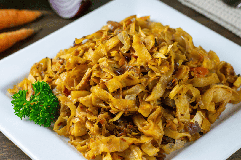 A bright, high-angle shot of a classic Kottu Roti on a square white plate, garnished with a sprig of fresh parsley.