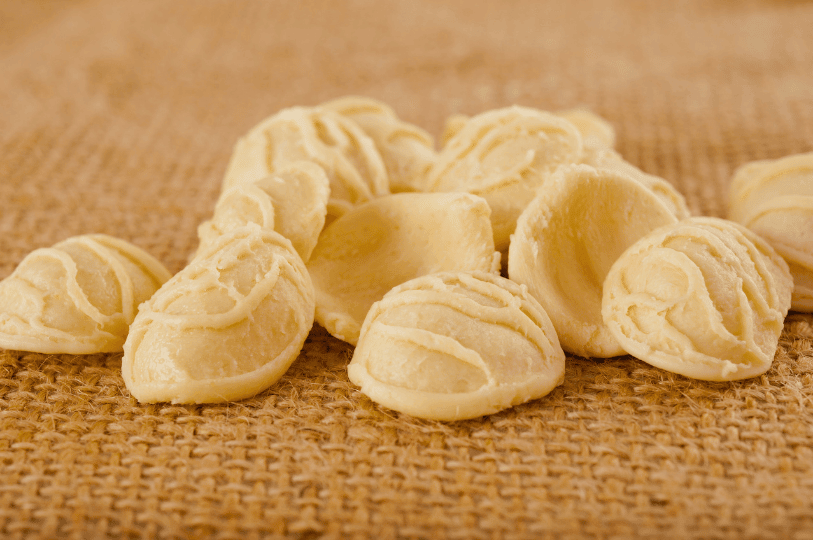 Uncooked orecchiette pasta, shaped like small, rough-textured bowls or "little ears," a famous specialty of Puglia, resting on a burlap cloth.