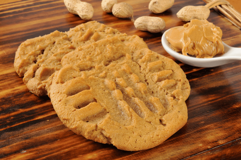A top-down perspective of cookies scattered on a wooden table, showcasing the uniform circular shape and the distinct fork indentations on top.