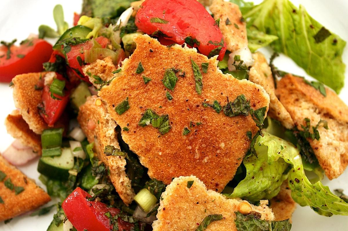 Close-up of an authentic Fattoush salad with large pieces of crispy, fried or baked pita bread, fresh chopped tomatoes, cucumbers, green onions, mint, and romaine lettuce.