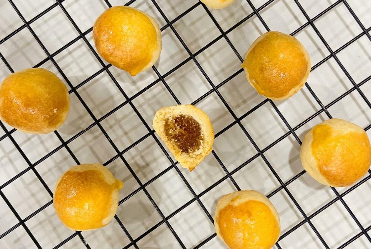 Round pineapple pastry balls cooling on a wire rack, with one cut in half.