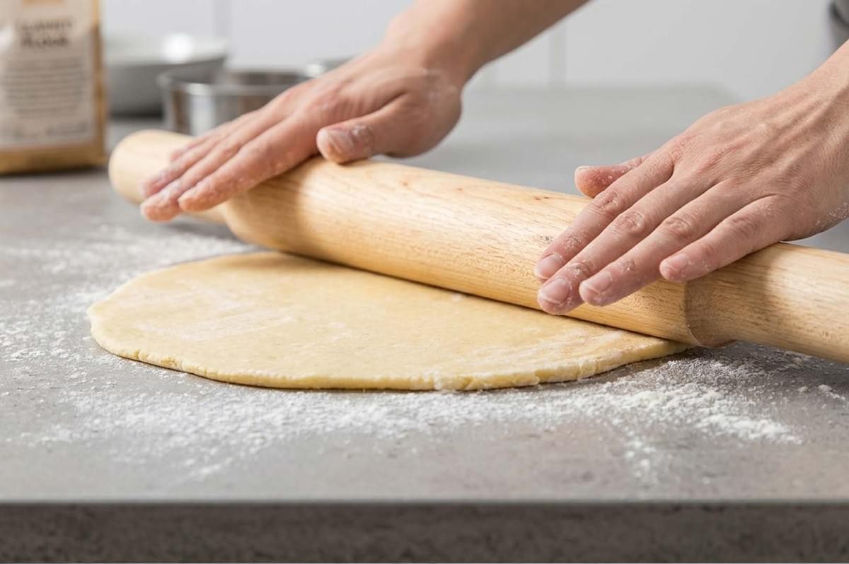 Hands rolling out dough on a floured surface