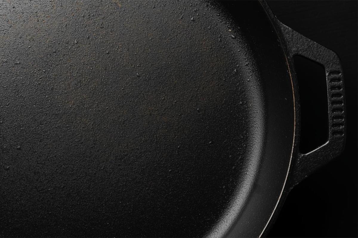Extreme close-up of the rough, textured surface of a well-seasoned, matte black cast iron skillet.