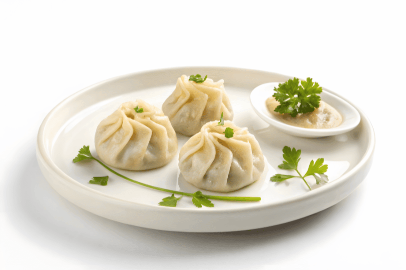 Three steamed dumplings arranged in a triangle on a white plate, each topped with herbs and paired with a dipping sauce—reflecting the elegant simplicity of dumplings across cultures, from Chinese dim sum to Polish pierogi.