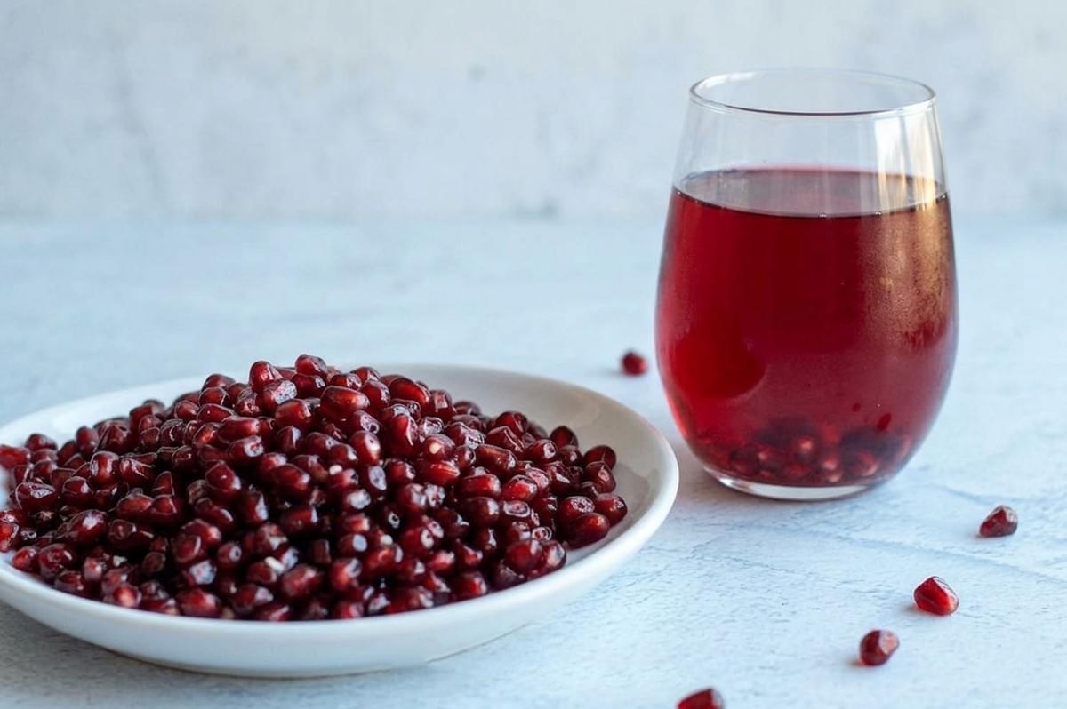 Plate of pomegranate seeds next to a glass of fresh pomegranate juice