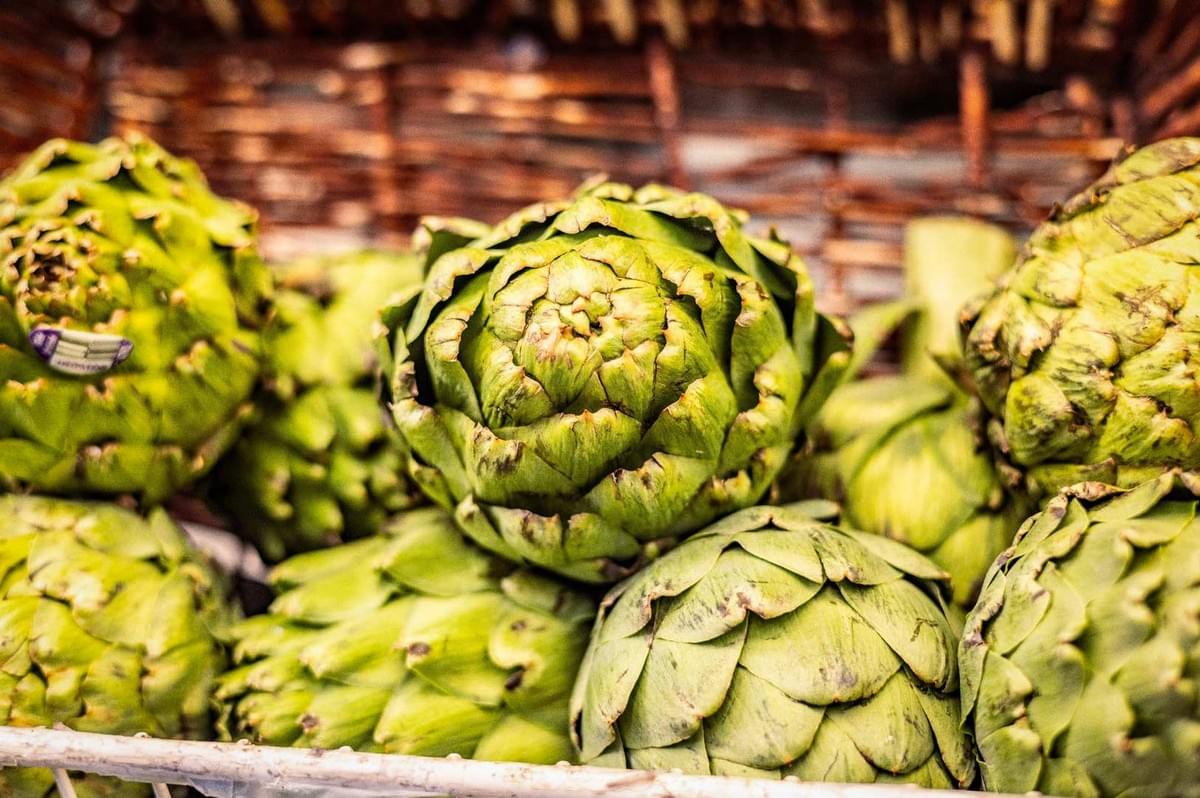A close-up view of fresh green artichokes arranged in a basket, showing tightly layered leaves and natural texture.