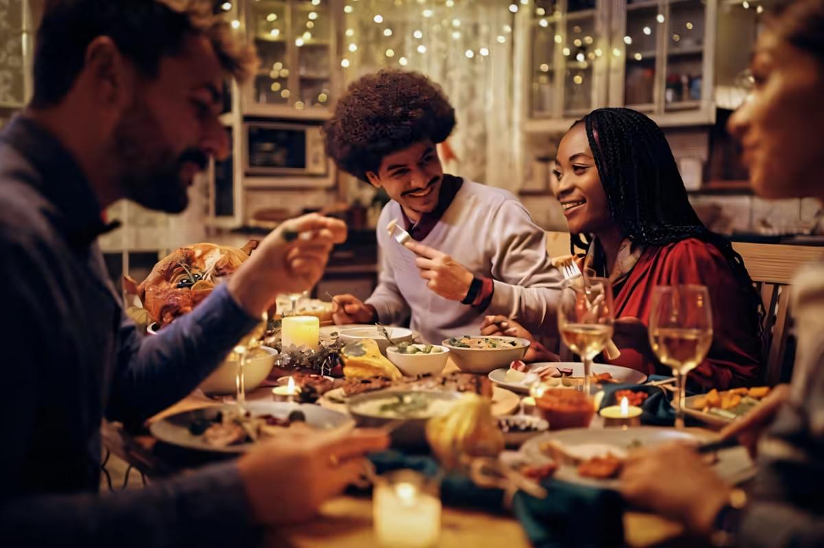 Cozy holiday dinner table with candles, plated dishes, and people enjoying a festive meal.
