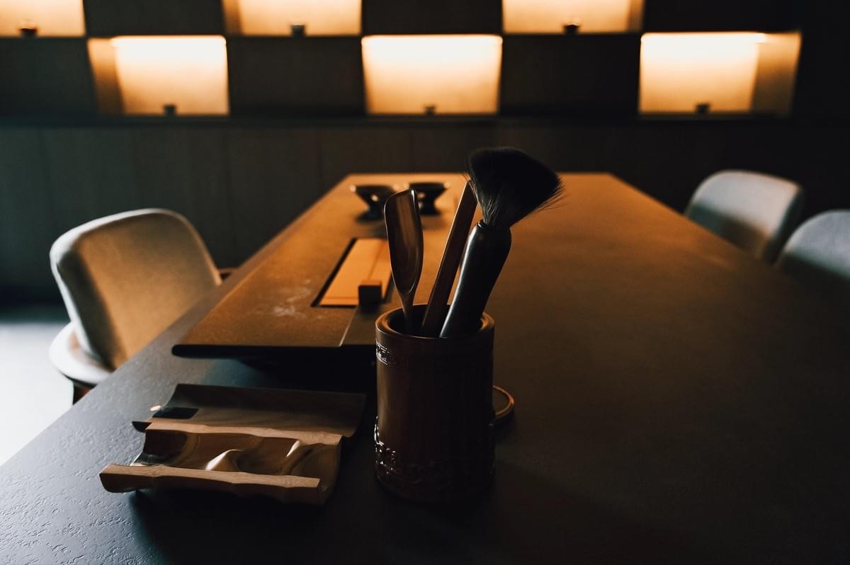 Low‑angle, shallow‑depth-of-field shot of a minimalist tea table with wooden tea tools and a brush holder, set in a warmly lit, modern tea room interior.