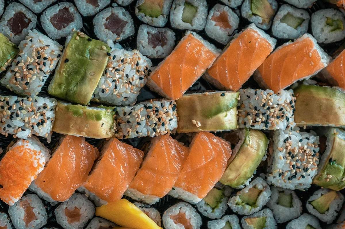 Assorted sushi platter with salmon-topped rolls, avocado slices, sesame seeds, and seaweed-wrapped maki arranged on a wooden board for Japanese cuisine photography.