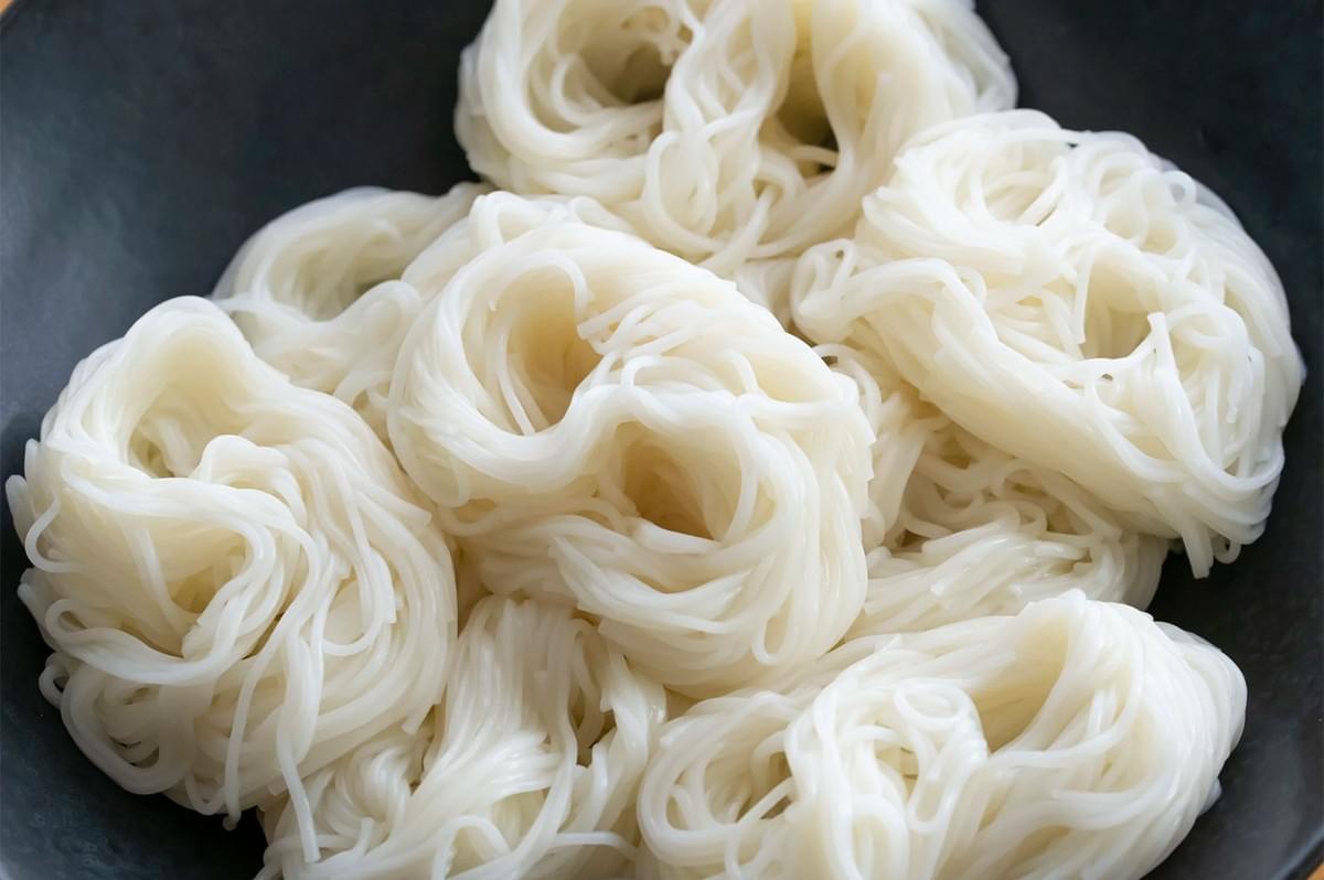 Freshly boiled white Japanese somen noodles arranged in neat, circular serving bundles on a dark plate.