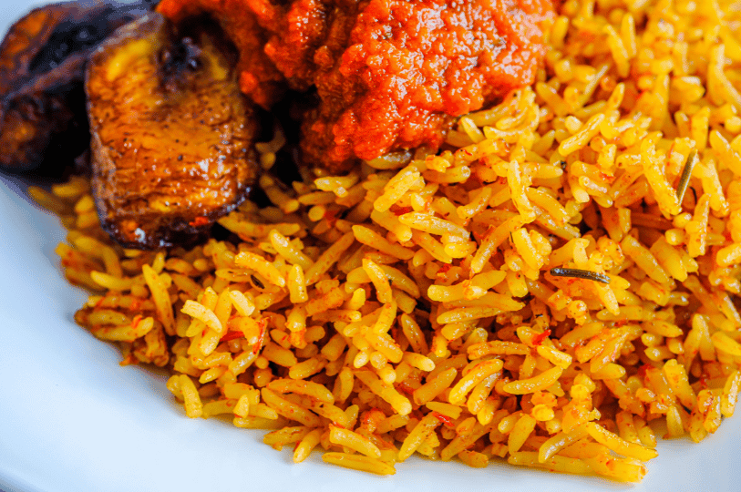 A macro close-up of fluffy Jollof rice grains glistening with savory stew oils, highlighting the textured, spicy coating and garnished with a sprig of fresh thyme.