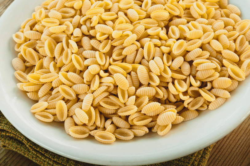 A white plate overflowing with uncooked malloreddus (also known as gnocchetti sardi), a small, ridged, shell-like pasta native to Sardinia.