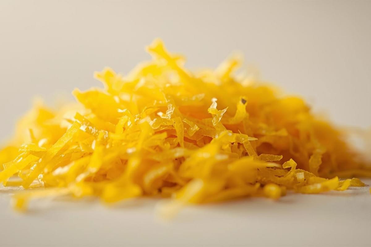 Extreme close-up, shallow depth of field shot of a mound of bright yellow, finely shredded lemon or orange zest, resting on a light surface.