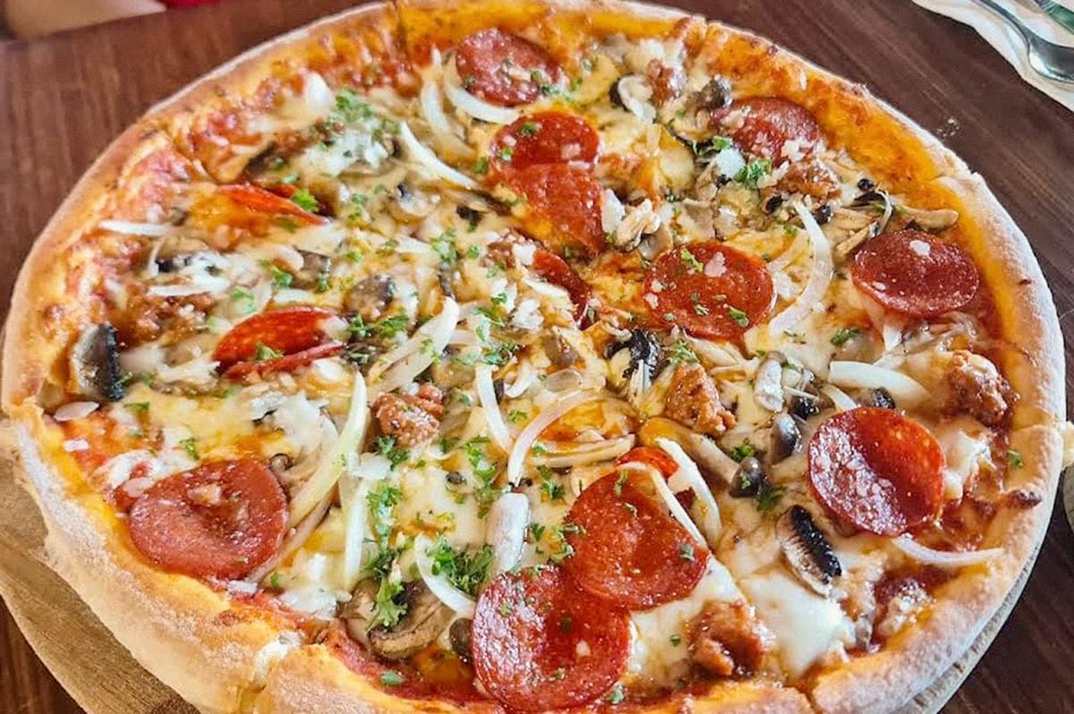 A loaded pizza topped with pepperoni, mushrooms, onions, sausage, melted cheese, and herbs on a wooden table.