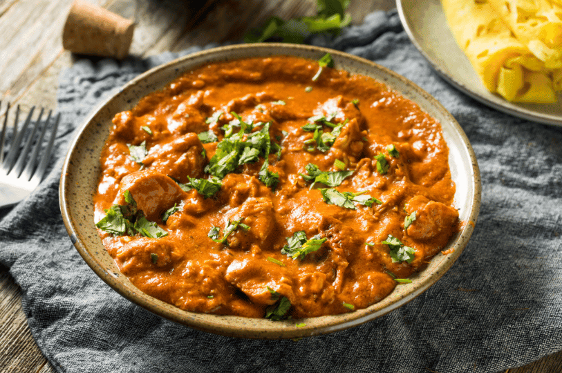 A rustic bowl of butter chicken in creamy tomato curry, garnished with cilantro and served alongside golden flatbread—evoking the bold flavors and cozy charm of Indian home cooking.