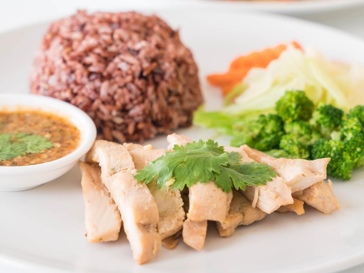 A close up shot of a chicken rice dish with brown rice and vegetables.