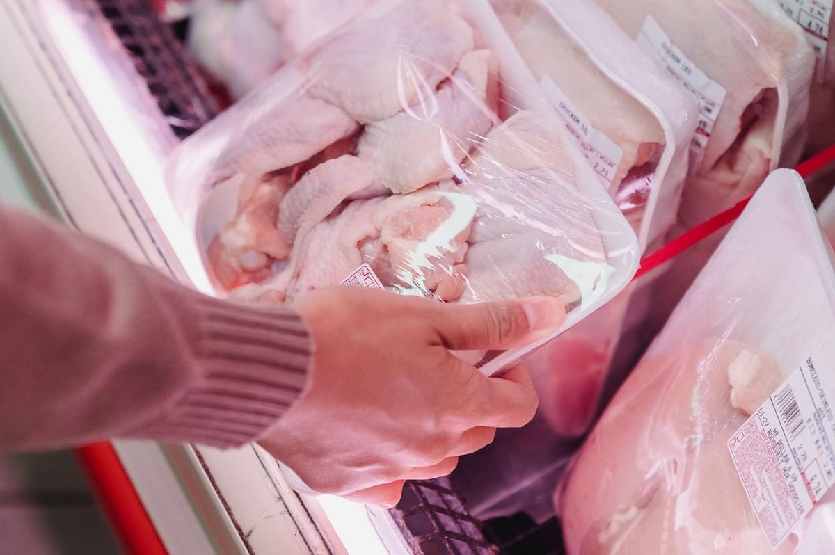 Person holding raw chicken meat packet in a supermarket aisle to check for halal certification.