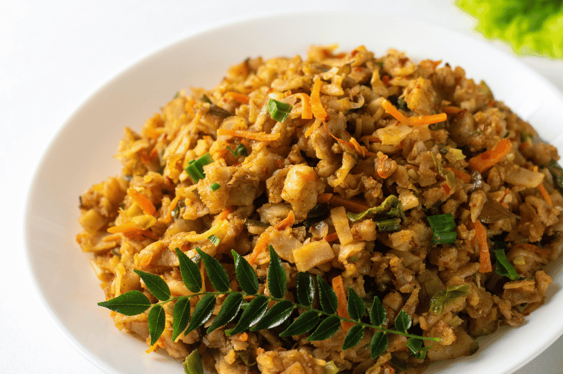 A bowl of Kottu Roti mixed with shredded carrots and green onions, decorated with a fresh curry leaf sprig on a clean white background.
