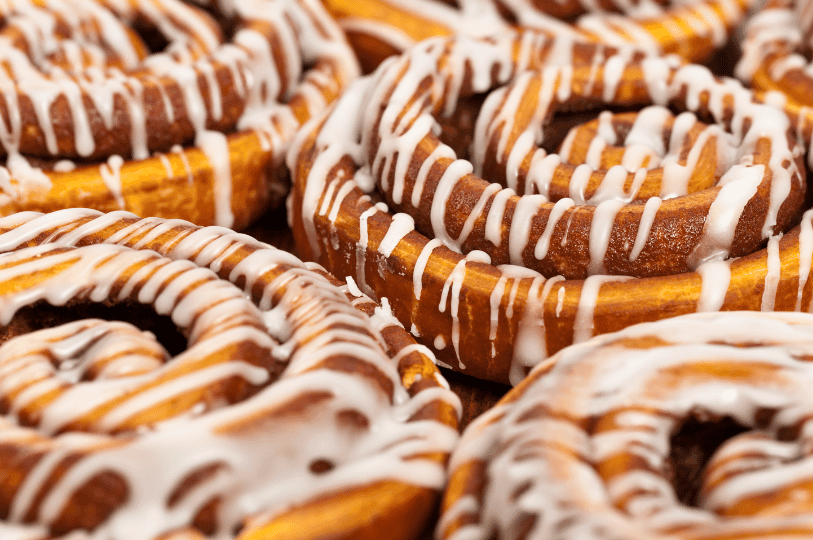 Extreme close-up of the spiral layers of several cinnamon rolls, showcasing the dark cinnamon-sugar filling and the thin, drizzled icing.
