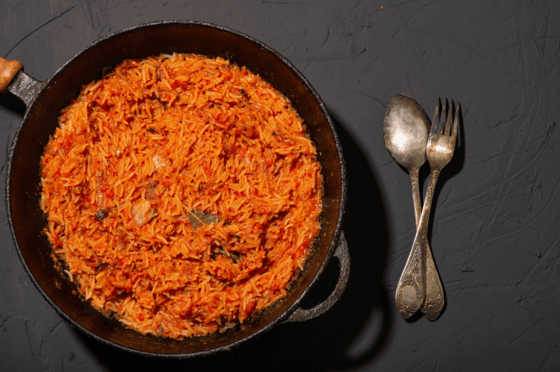 A rustic presentation of steaming Jollof rice in a traditional cast-iron pot, showcasing the deeply flavorful, slightly charred bottom layer known as the highly coveted "party rice."