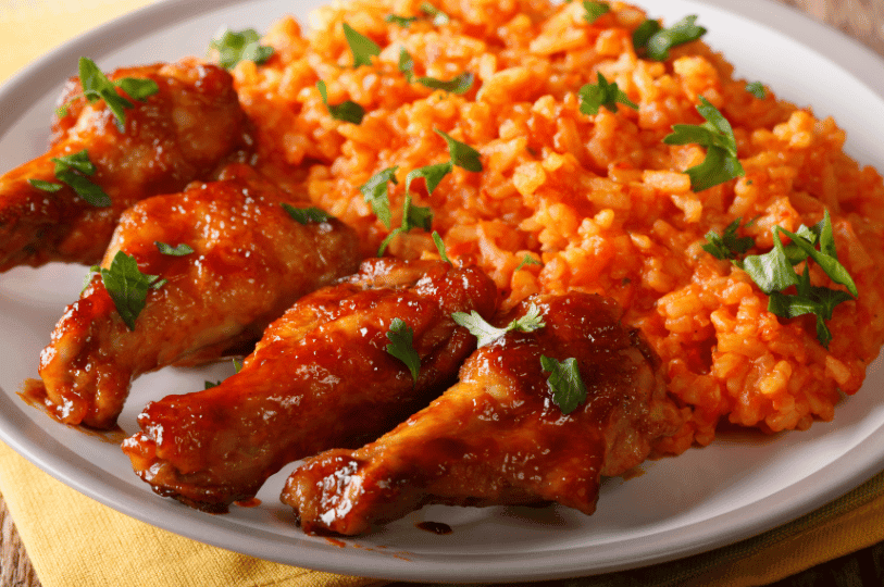 A vibrant plate of West African Jollof rice, showcasing its signature deep reddish-orange color from the rich tomato and pepper base, served with a side of caramelized fried plantains and grilled chicken.