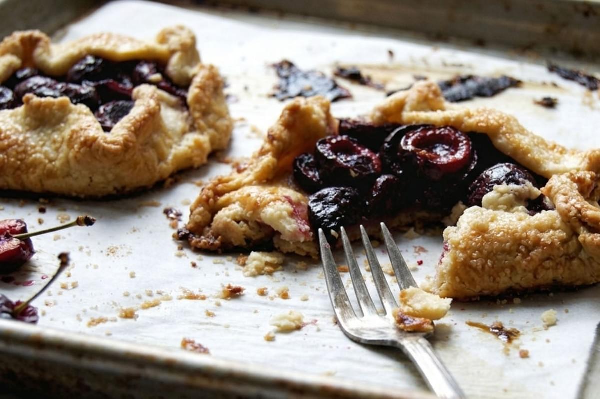 Partially eaten cherry galette with flaky crust and fork on parchment paper