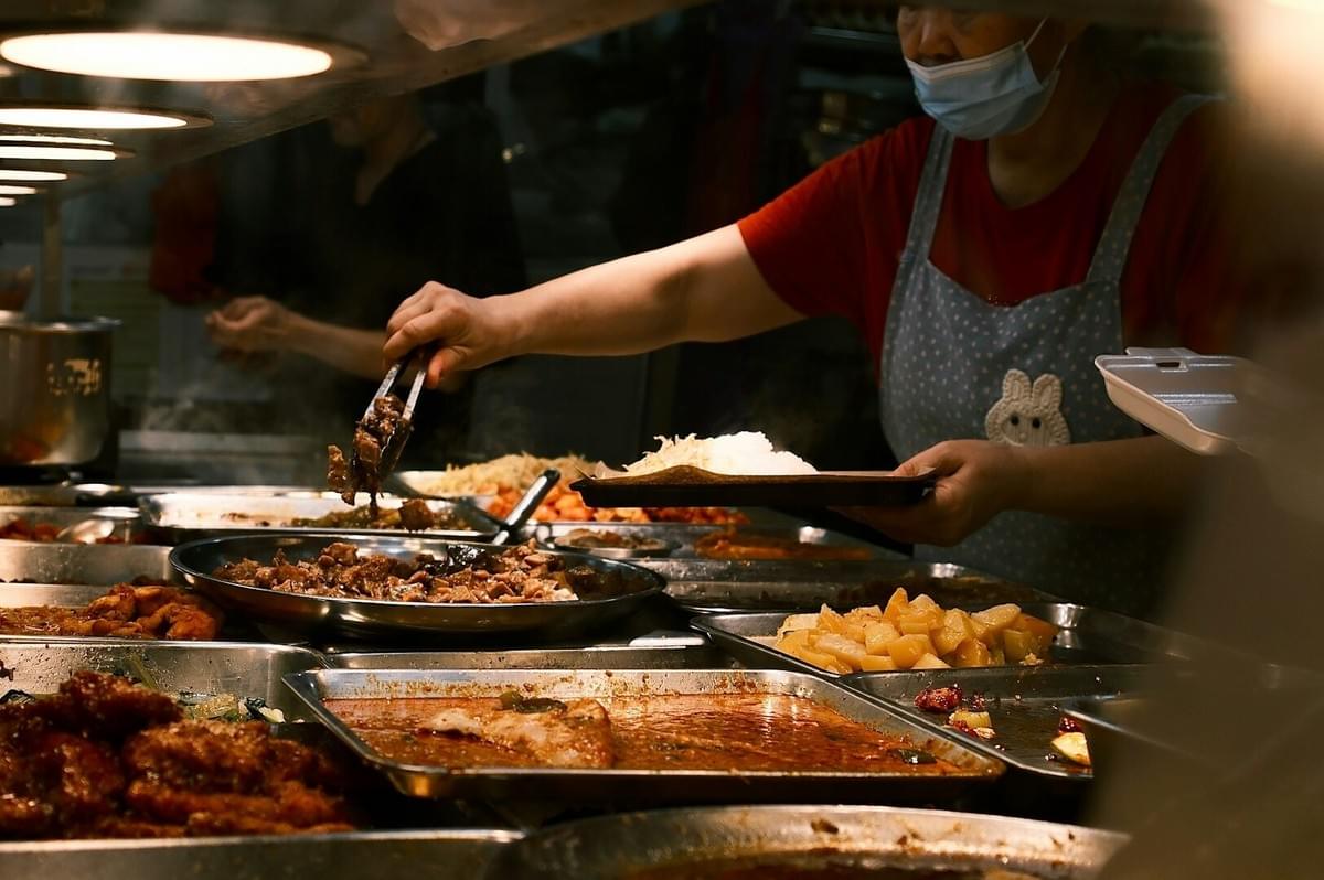 A masked woman serving food in a restaurant, showcasing her skills as a chef in Singapore.