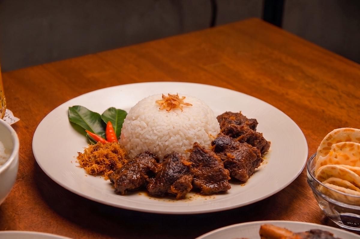 Beef Rendang with white rice served on a white plate with chili and kaffir lime leaves.