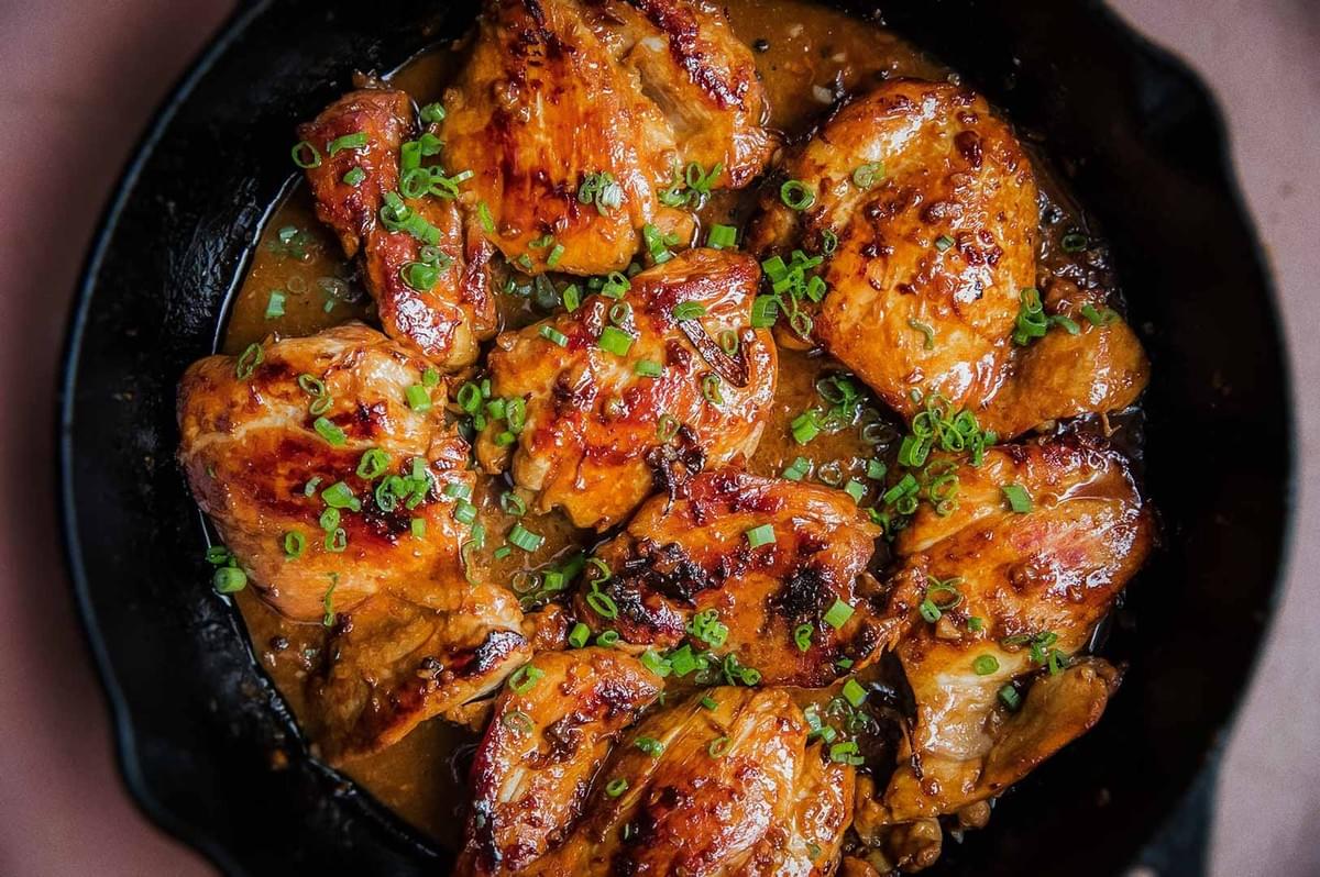 Filipino chicken adobo in skillet, glazed with soy-vinegar sauce and garnished with chopped green onions.