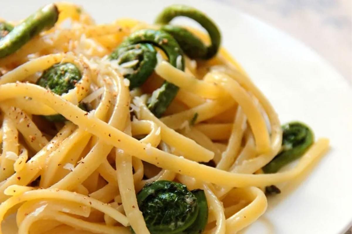 Delicious linguine pasta dish featuring sautéed green fiddlehead ferns, topped with grated parmesan cheese and black pepper.