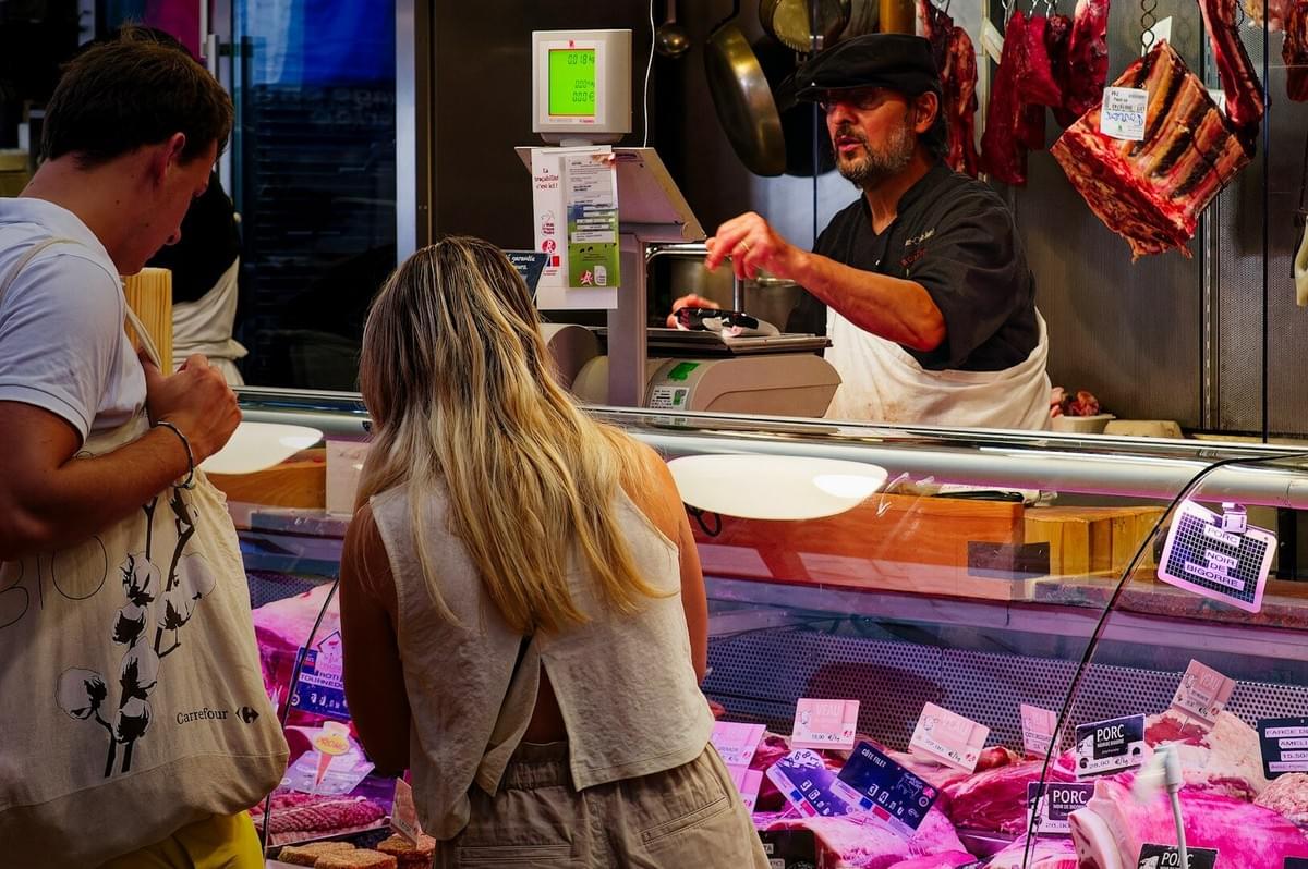 A man and woman examine various meats at a counter, engaging with local food culture in an unfamiliar setting.
