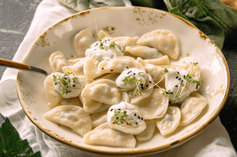 A close-up of soft, boiled pierogi garnished with sesame seeds and microgreens, highlighting a modern, light presentation of the classic dumpling.