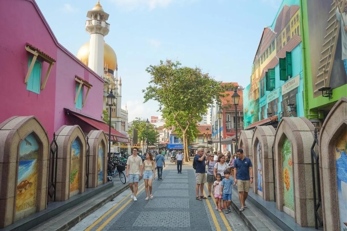 Tourists walking through the colorful streets of Kampong Glam in Singapore with the Sultan Mosque in the background.