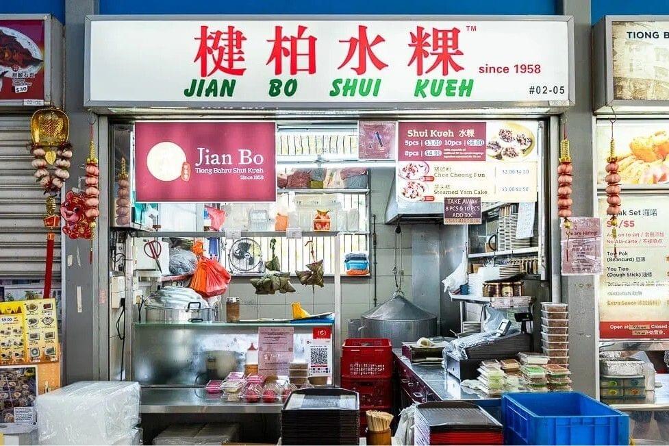 This image shows the storefront of Jian Bo Shui Kueh, a traditional food stall established in 1958 located at stall #02-05. The stall features a prominent white sign with red and green lettering, displaying a menu that specializes in shui kueh, chee cheong fun, and steamed yam cake.
